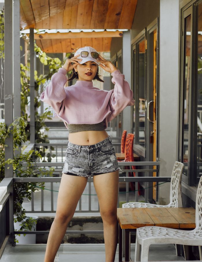 Trendy woman in a crop top and shorts poses confidently on a porch, showcasing modern fashion.