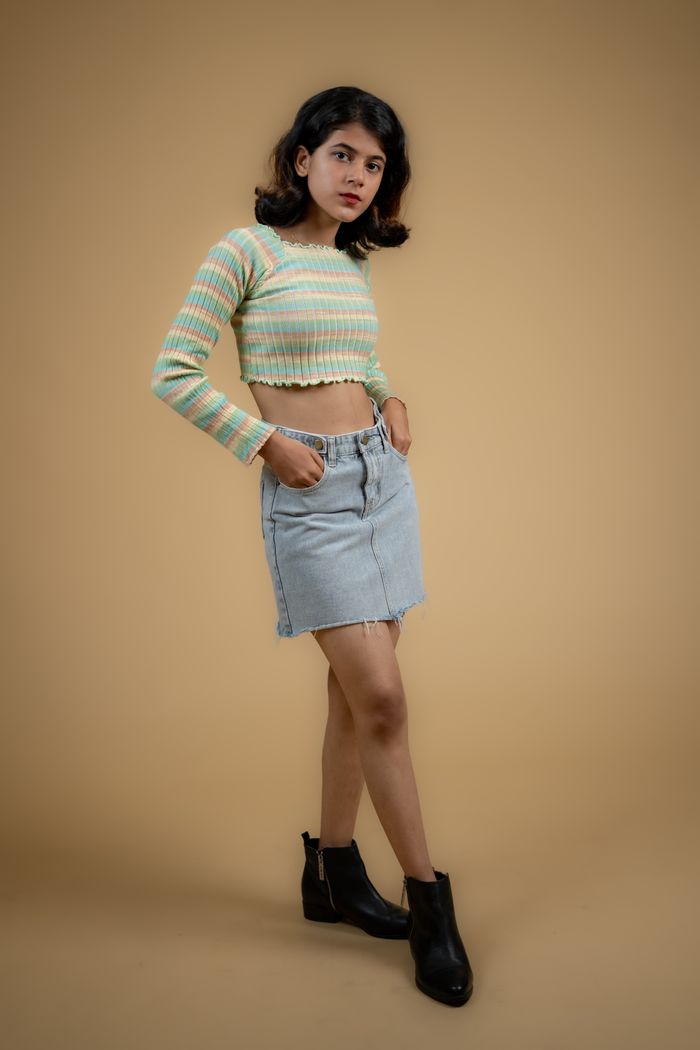 Trendy young woman posing in a studio wearing a crop top and denim skirt, showcasing modern fashion.