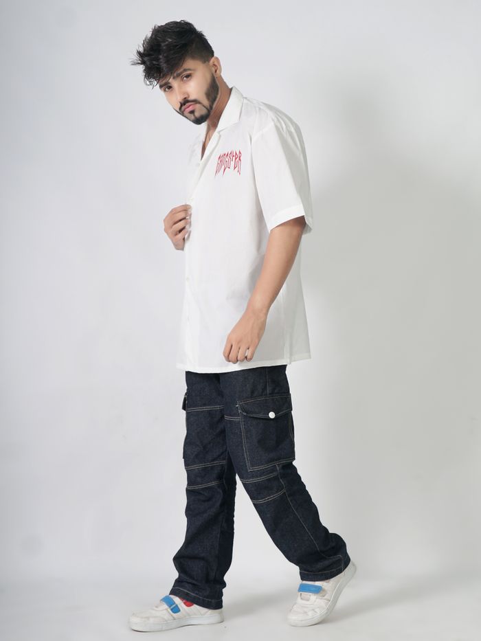 Studio shot of a man in a white shirt and denim pants posing fashionably.