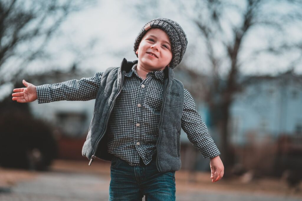 Joyful young boy smiling and posing in a winter setting, wearing a beanie and jacket.