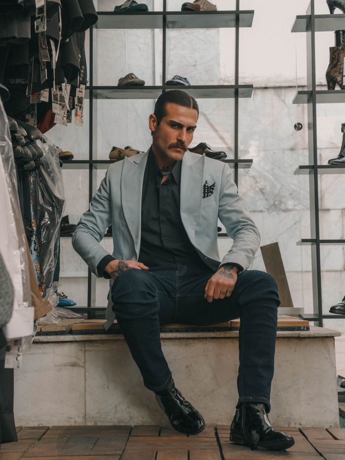 Man in suave outfit sitting in fashionable store, highlighting modern style and elegance.
